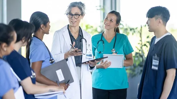A small group of medical professionals gathers in a hospital hallway for a training discussion, listening closely as the lead physician.