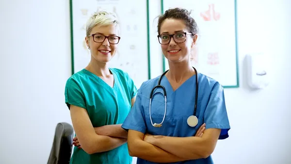 Two confident nurses standing with arms crossed in a modern medical office, representing nursing career growth, staffing goals, and professional advancement in today’s healthcare workforce.