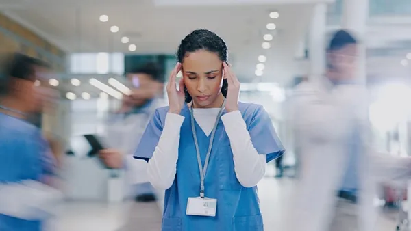 Nurse and woman with headache in hospital, stressed by a medical mistake, overwork, and burnout. Motion blur shows a healthcare worker experiencing migraines in a busy clinic, overwhelmed by fatigue, crisis, and frustration amid chaos.